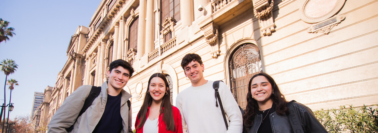 Grupo de estudiantes sonríe frente a la facha del Campus Casa Central UC.