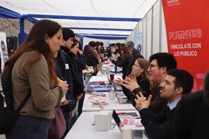 Feria laboral con stands informativos y asistentes interactuando bajo una carpa blanca en espacio abierto.