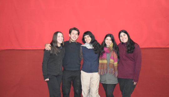 Grupo de cinco personas sonrientes frente a fondo rojo, transmitiendo unión y alegría.