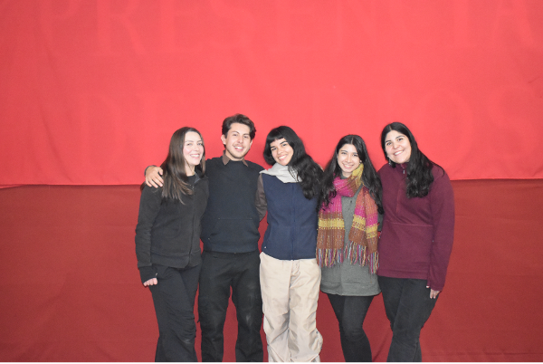 Grupo de cinco personas sonrientes frente a fondo rojo, transmitiendo unión y alegría.