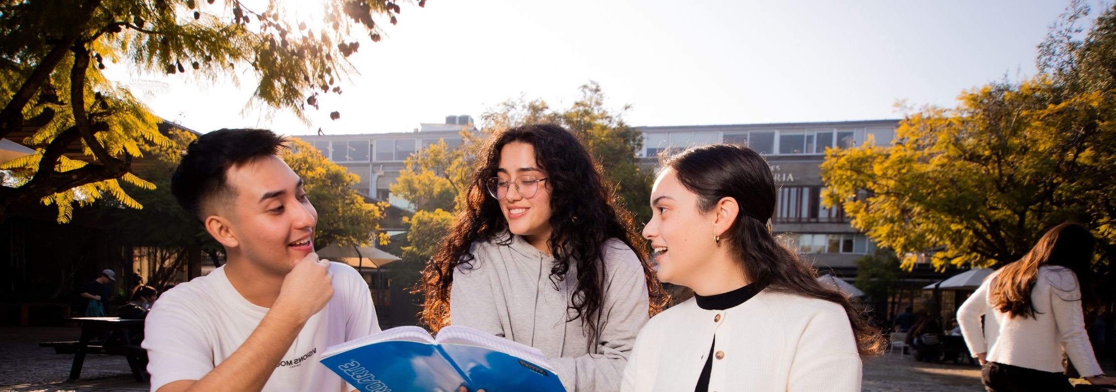 Tres estudiantes conversan con un cuaderno en la mano.
