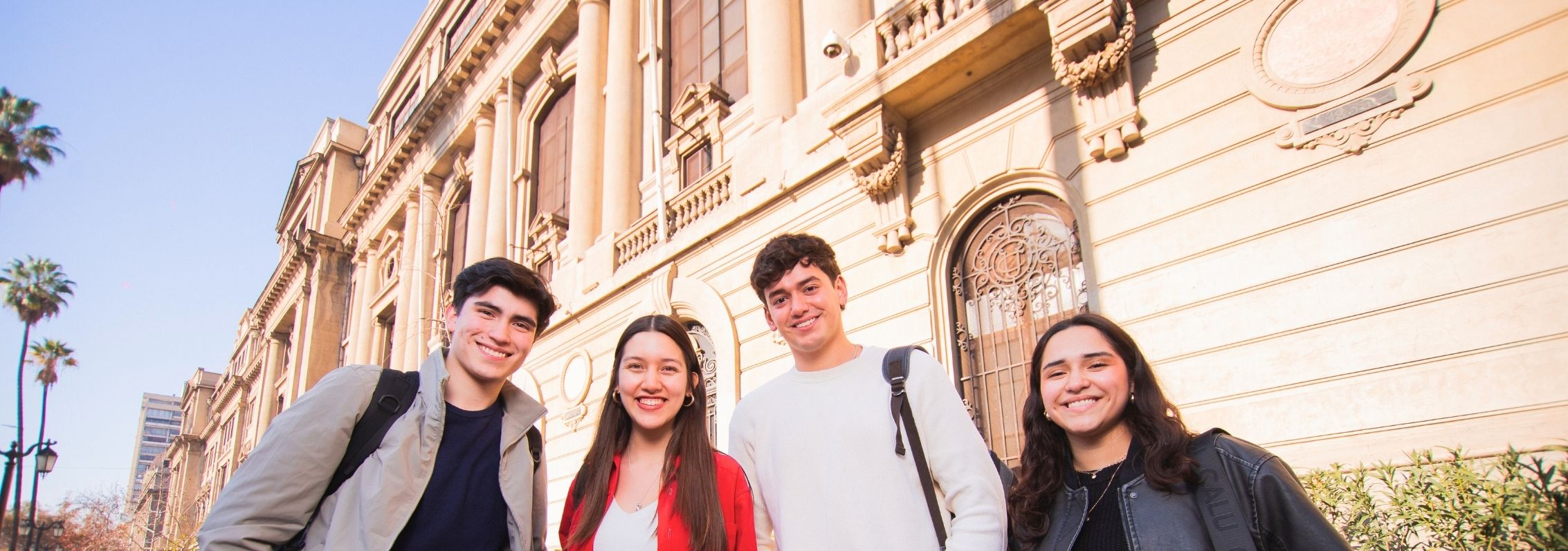 Cuatro estudiantes sonríen frente al Campus Casa Central.